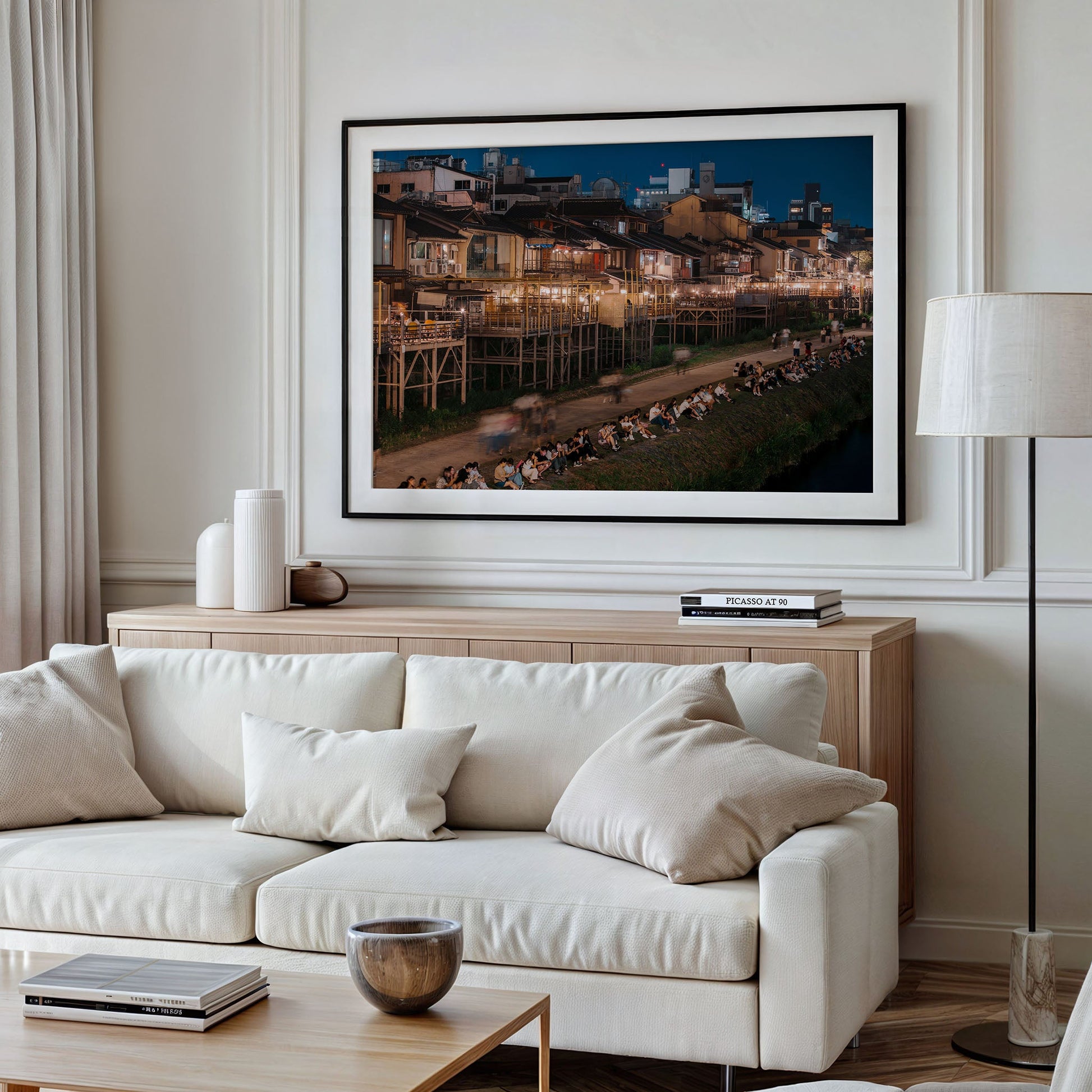 A modern living room with the Kamo River cream sofa, cushions, a wooden sideboard, and a large framed cityscape photo.