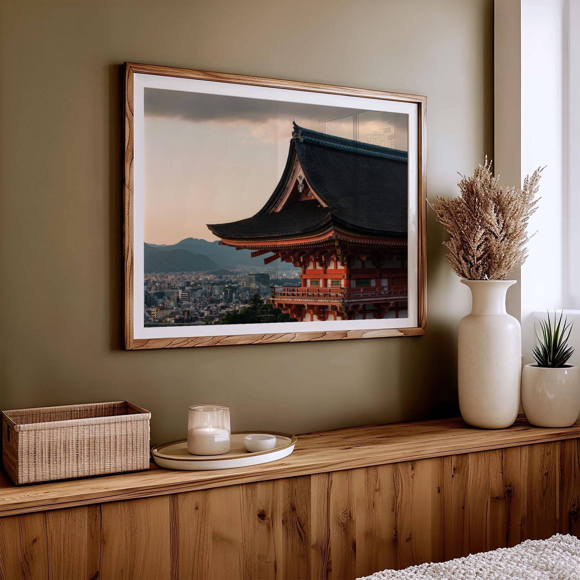 The Kiyomizu-dera Sunset III framed photo of a traditional Japanese roof hangs above a wooden console adorned with a vase and candle.