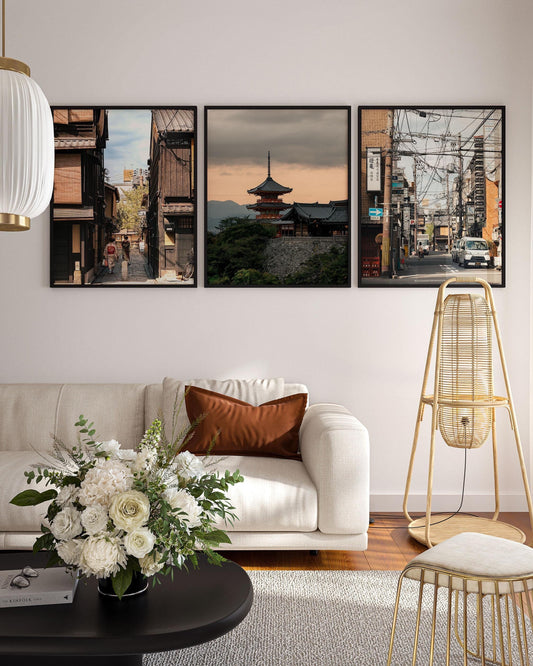 In a cozy living room: white sofa, brown cushion, table vase, & three framed Kyoto Allure cityscape photos on the wall.