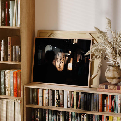 A bookshelf featuring the Kyoto At Night framed image of illuminated lanterns, surrounded by various books and a decorative plant vase.