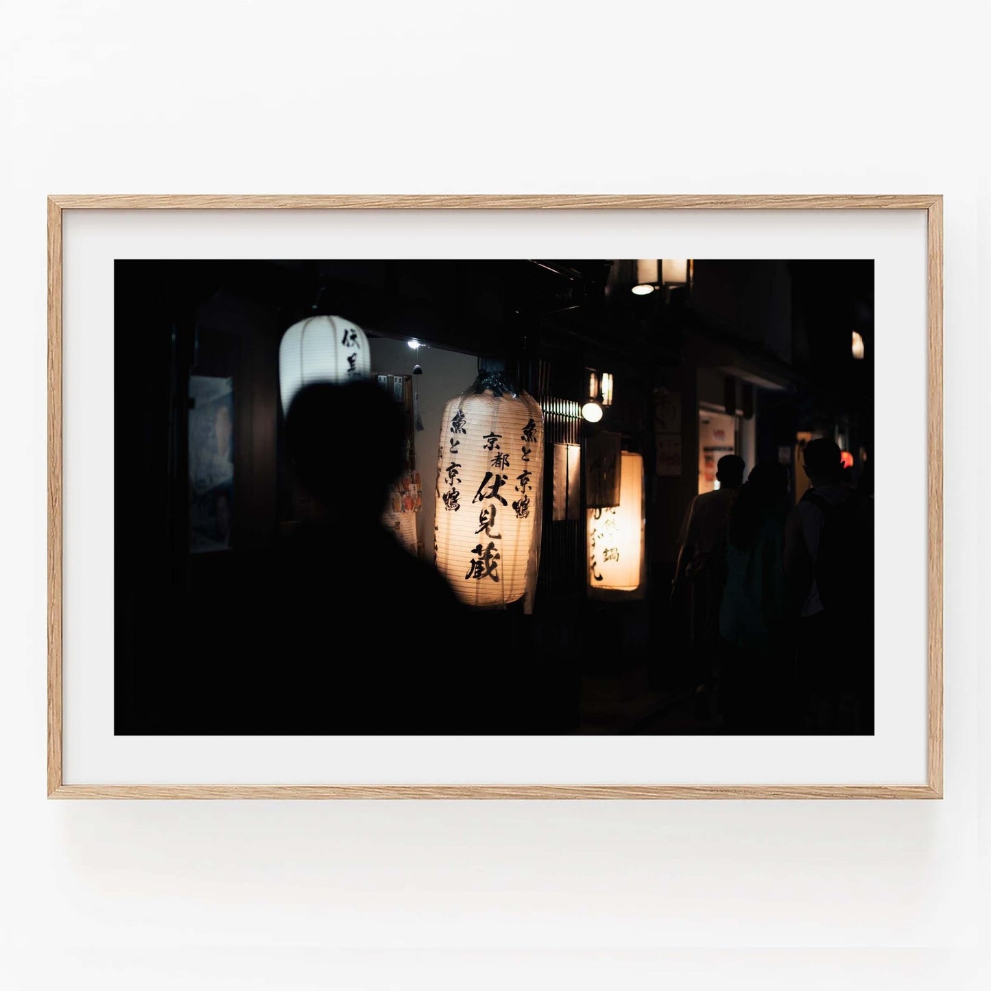 Kyoto At Night is a framed picture depicting a dark street scene illuminated by Japanese lanterns and silhouetted figures.