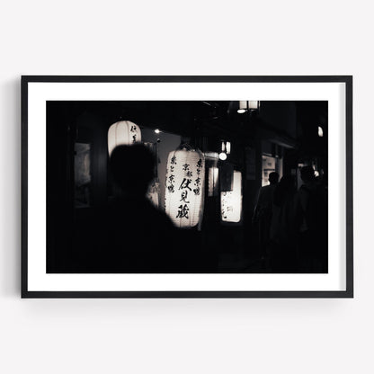 Silhouette of a person walking past illuminated lanterns with Japanese characters at night from the Kyoto At Night - Black and White collection.