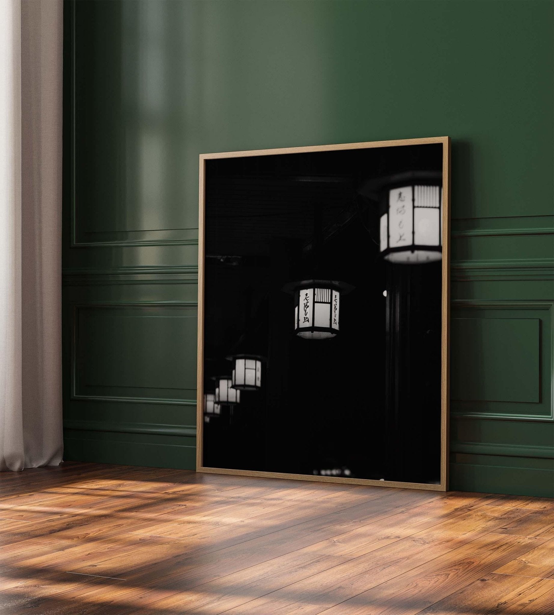 Framed photo titled Kyoto Lanterns II - Black and White leaning against a green paneled wall on a wooden floor.