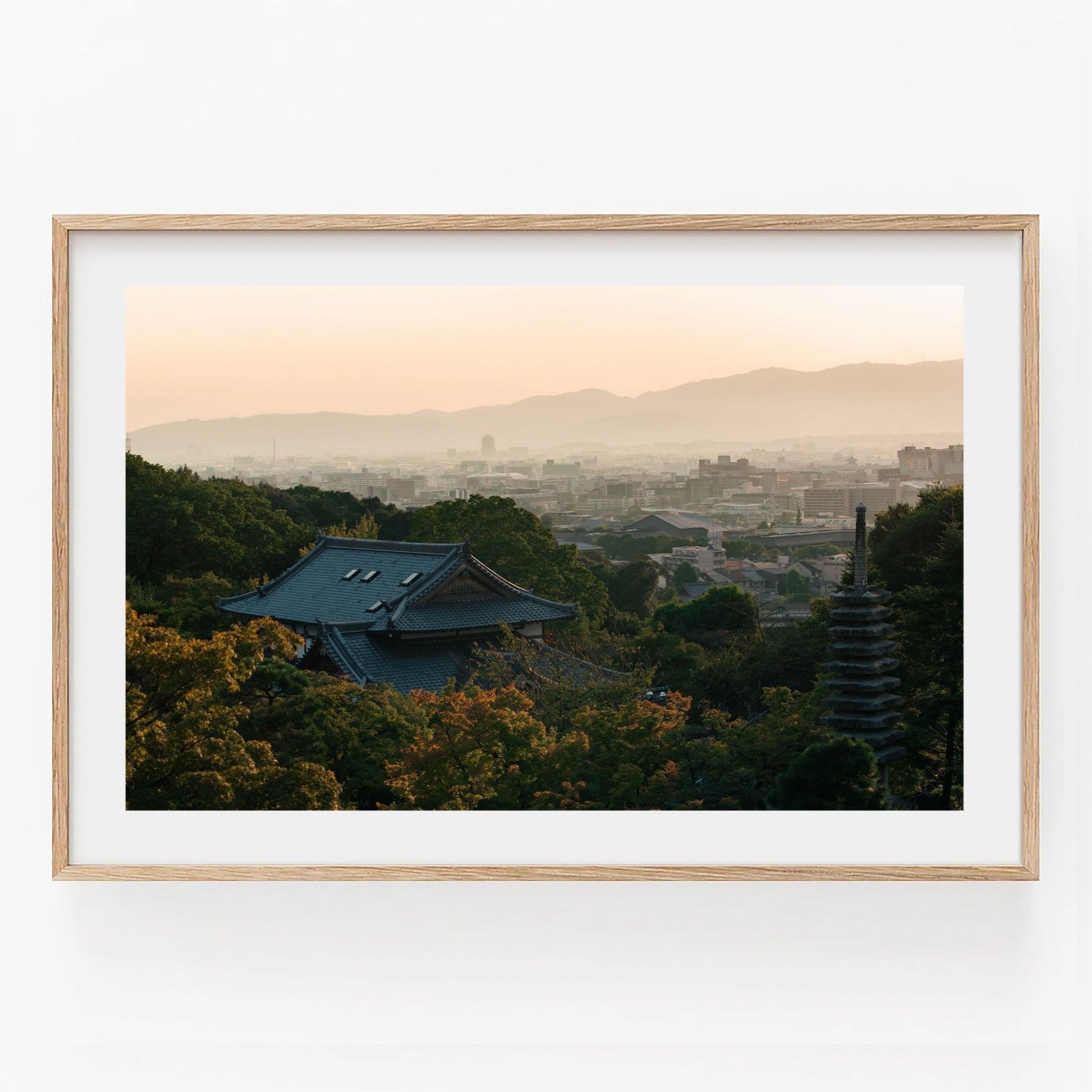 Framed photo titled Kyoto Sunset Skyline I, showcasing a serene landscape with a temple roof and pagoda surrounded by greenery at sunset.