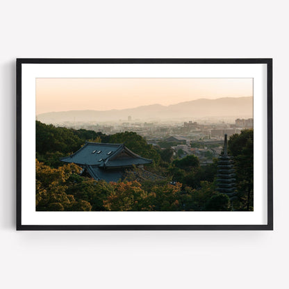 Framed photo titled Kyoto Sunset Skyline I, showcasing a Japanese landscape at sunset with rooftops, greenery, and distant mountains.