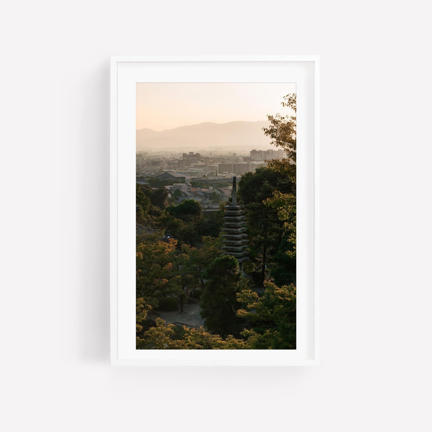 The framed photo titled Kyoto Sunset Skyline II features a distant pagoda against a hazy sunset and cityscape, surrounded by lush trees.