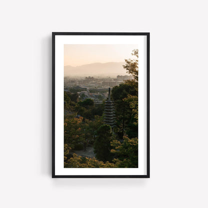 Kyoto Sunset Skyline II: A framed photo of a pagoda surrounded by trees with a cityscape and mountains in the background.