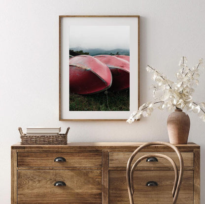 The Lake Kawaguchi Boats framed picture features overturned red boats, displayed on a wall above a wooden dresser, accompanied by a vase and chair.