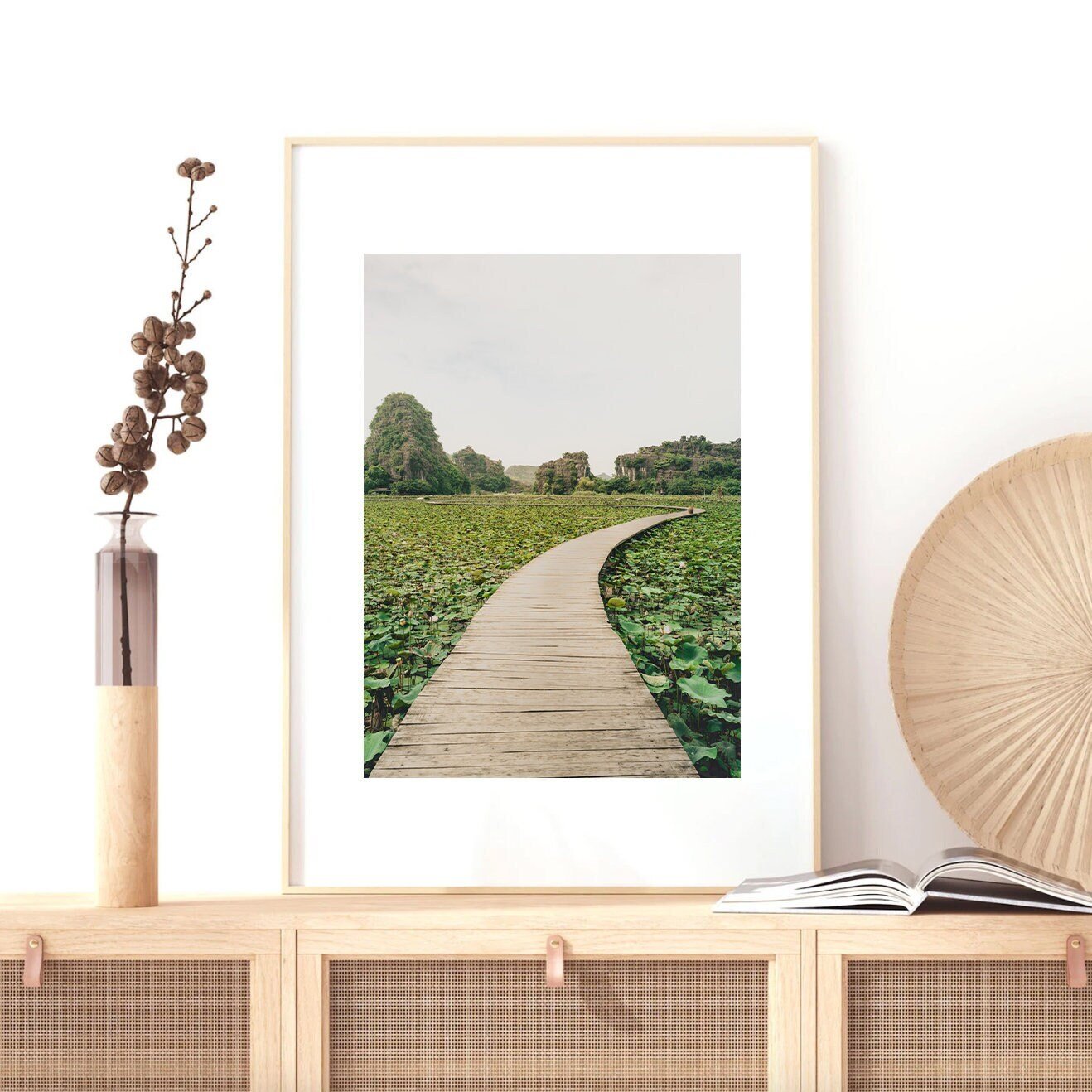 The Lead the Way framed photo showcases a wooden path through greenery, elegantly placed on a decorated wooden cabinet.