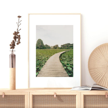 The Lead the Way framed photo showcases a wooden path through greenery, elegantly placed on a decorated wooden cabinet.