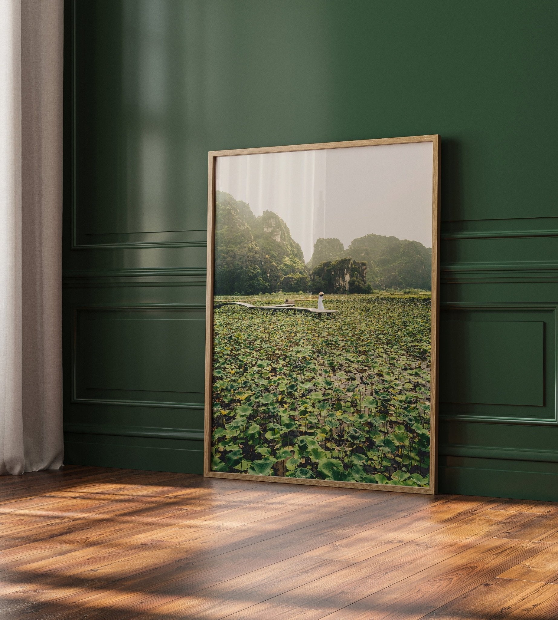 Lotus Lady painting framed, depicting a boat on a lake, rests against a green paneled wall.