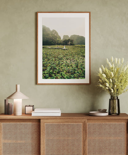 Lotus Lady photo above a wicker cabinet with books, lamp, and vase on a green wall.