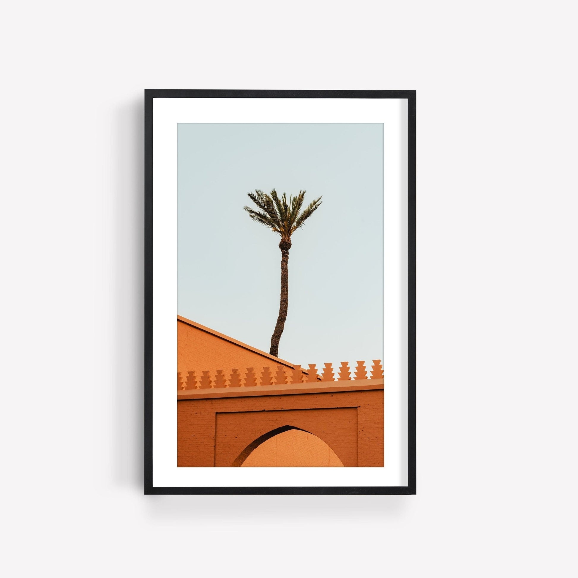 Framed Marrakesh Palm Tree photo shows a lone palm above an orange building with decorative trim on a light sky backdrop.