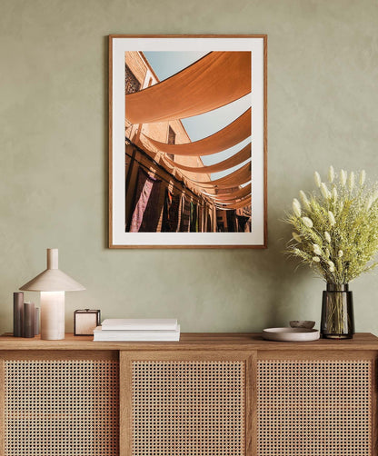 Minimalist interior with Marrakesh Souk II wall art, a wicker sideboard, books, lamp, and a vase with white flowers.