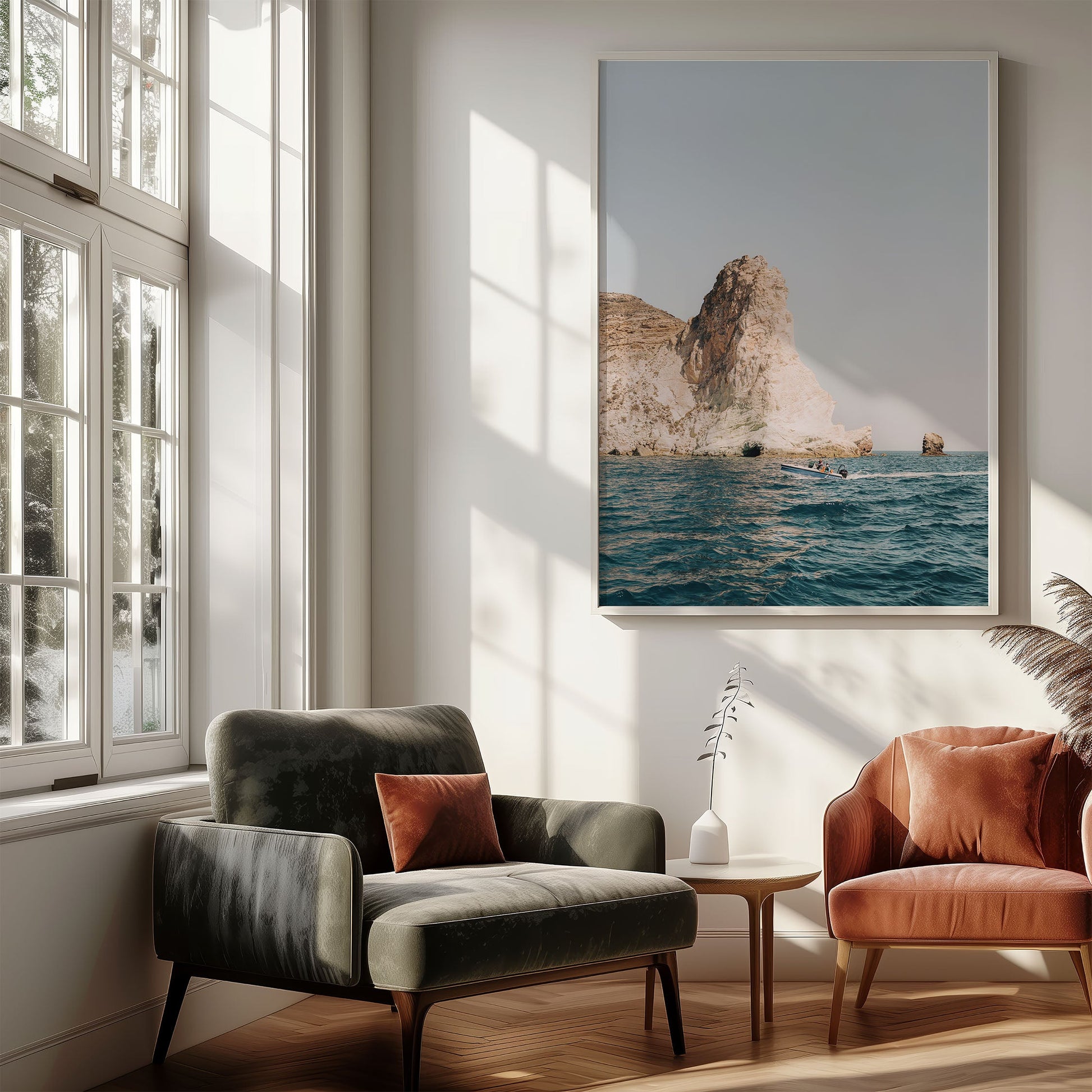 Sunny living room with two armchairs, a small table, and Mediterranean Adventure wall art above blue water.