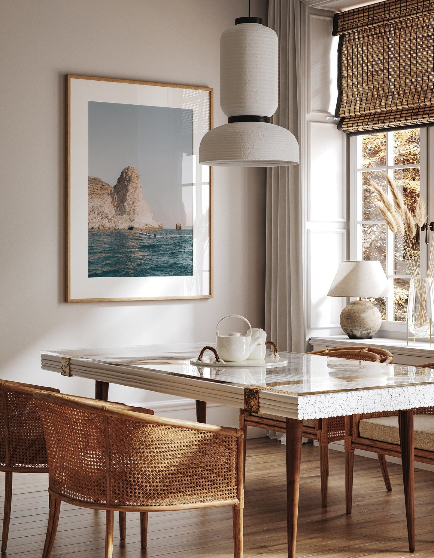 A sunlit dining room with a marble table, wicker chairs, pendant lamp, and Mediterranean Adventure framed on the wall.