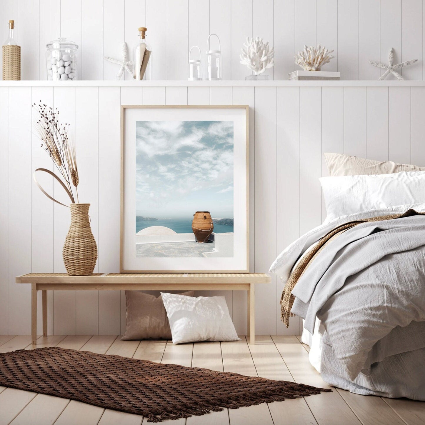 Cozy bedroom with neutral decor, featuring a bed, Mediterranean planter, bench, and framed sea view picture.