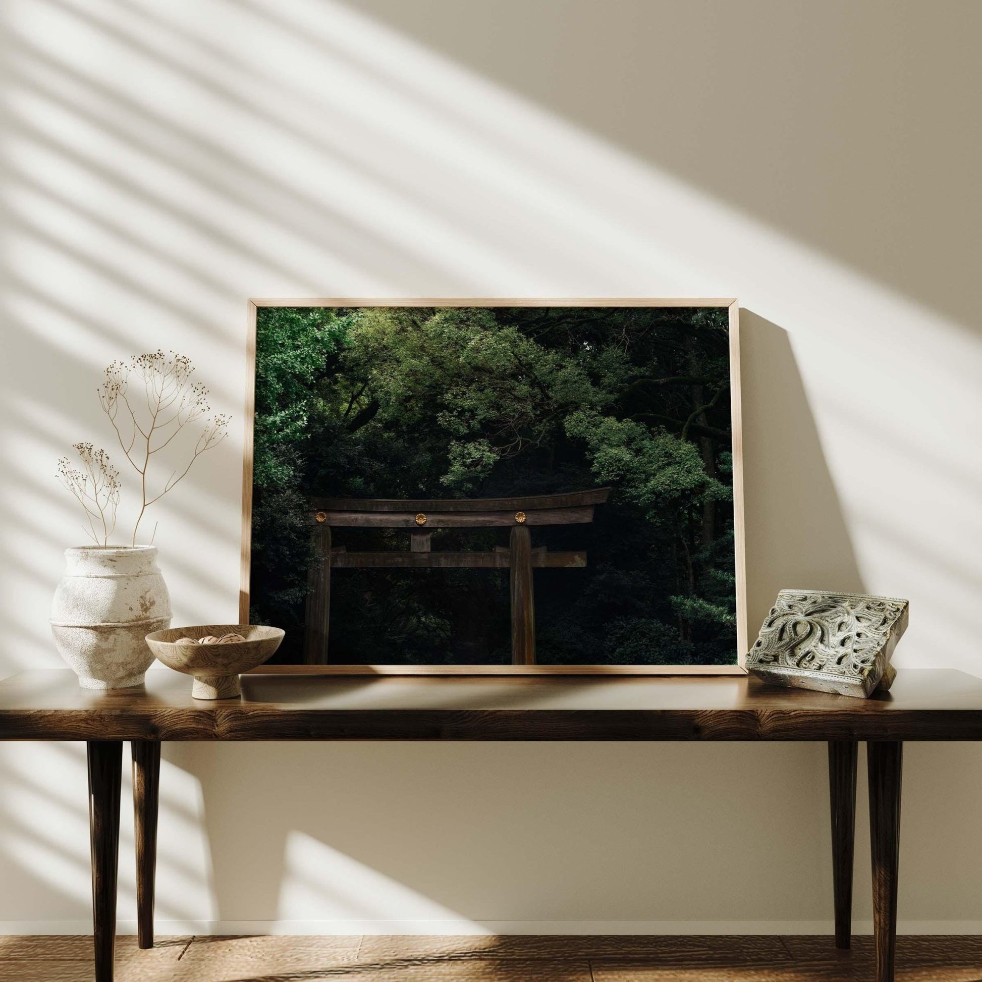 A framed photo titled Meiji Jingu Shrine of a torii gate among trees is displayed on a wooden table with vases in dappled sunlight.