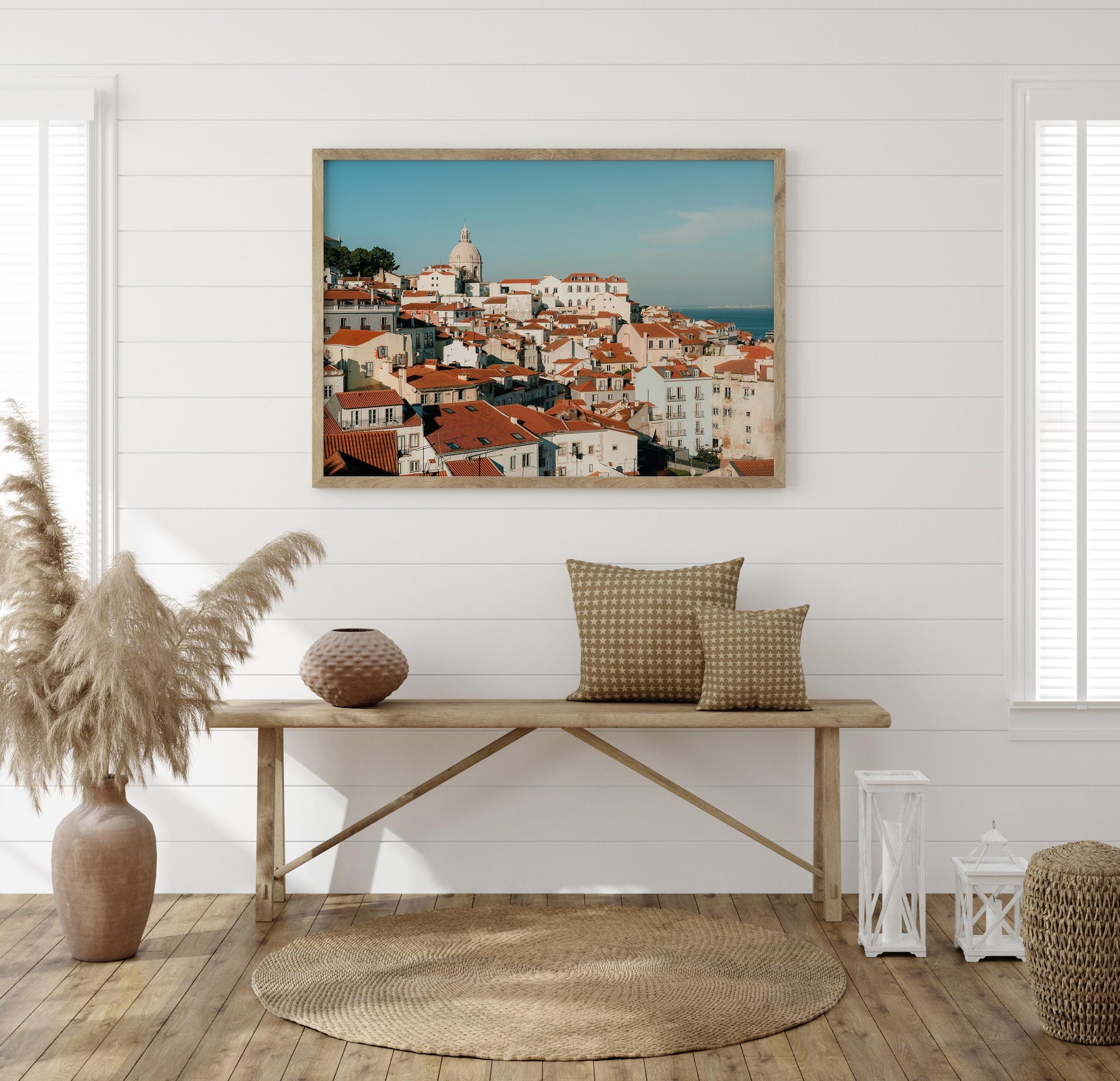 A cozy room with neutral decor, a wooden bench, pillows, pampas grass, and the Miradouro cityscape photo on the wall.