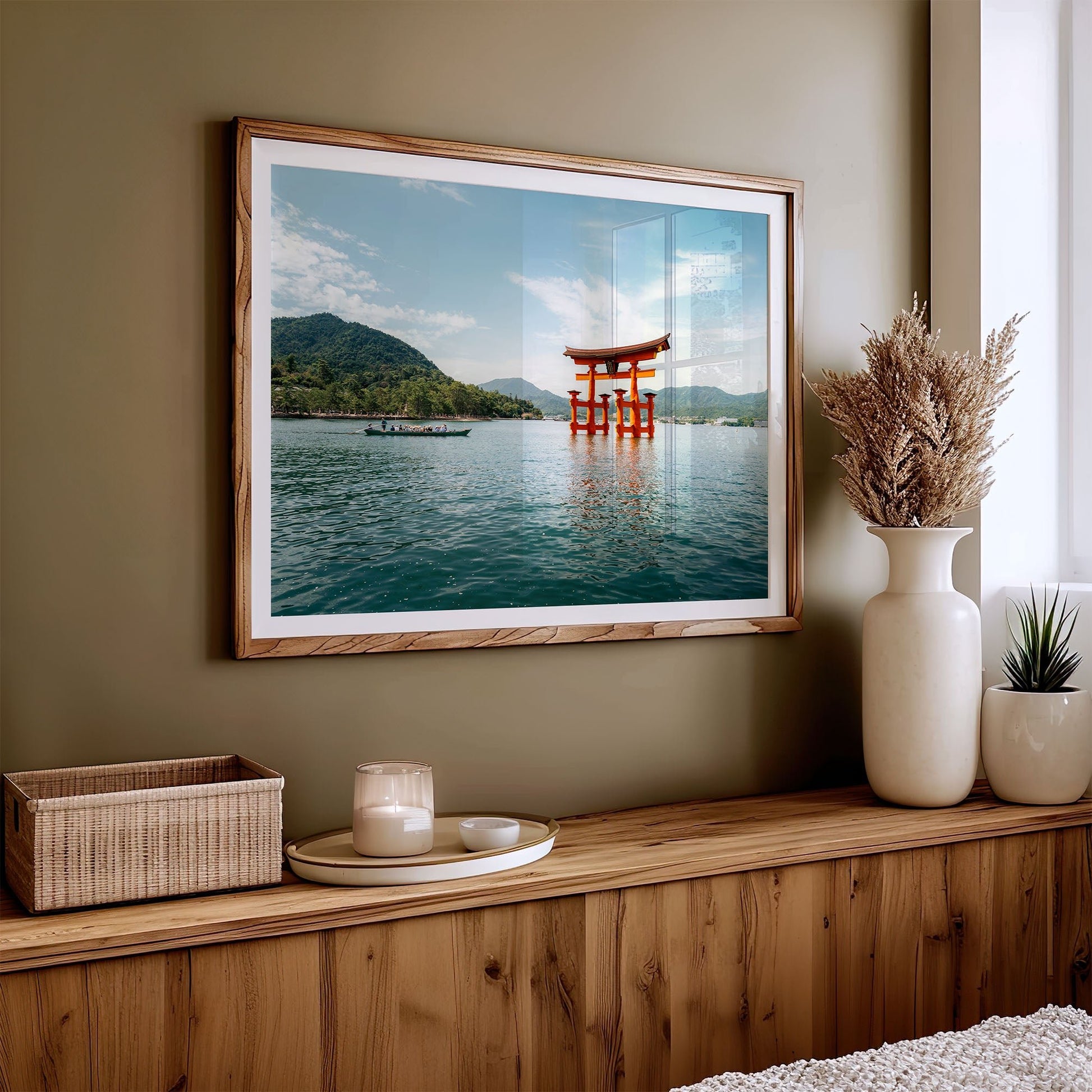 Miyajima Passage I framed photo on a shelf with a basket, candle, and vases in a room with green walls.