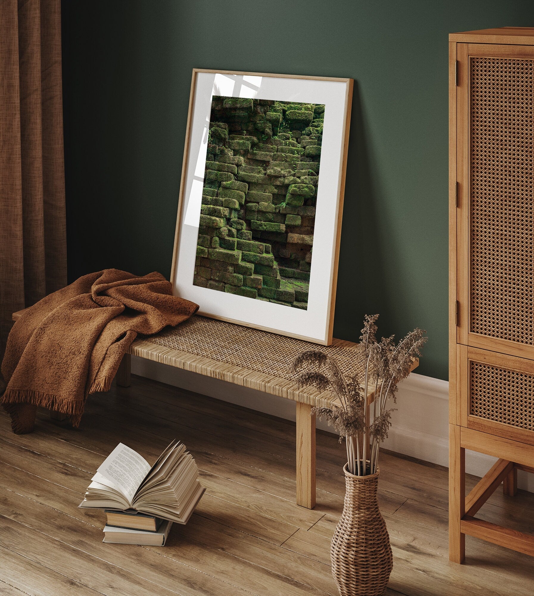 The Mossy Elegance picture rests on a woven bench with a blanket and open book beside it in a cozy room.