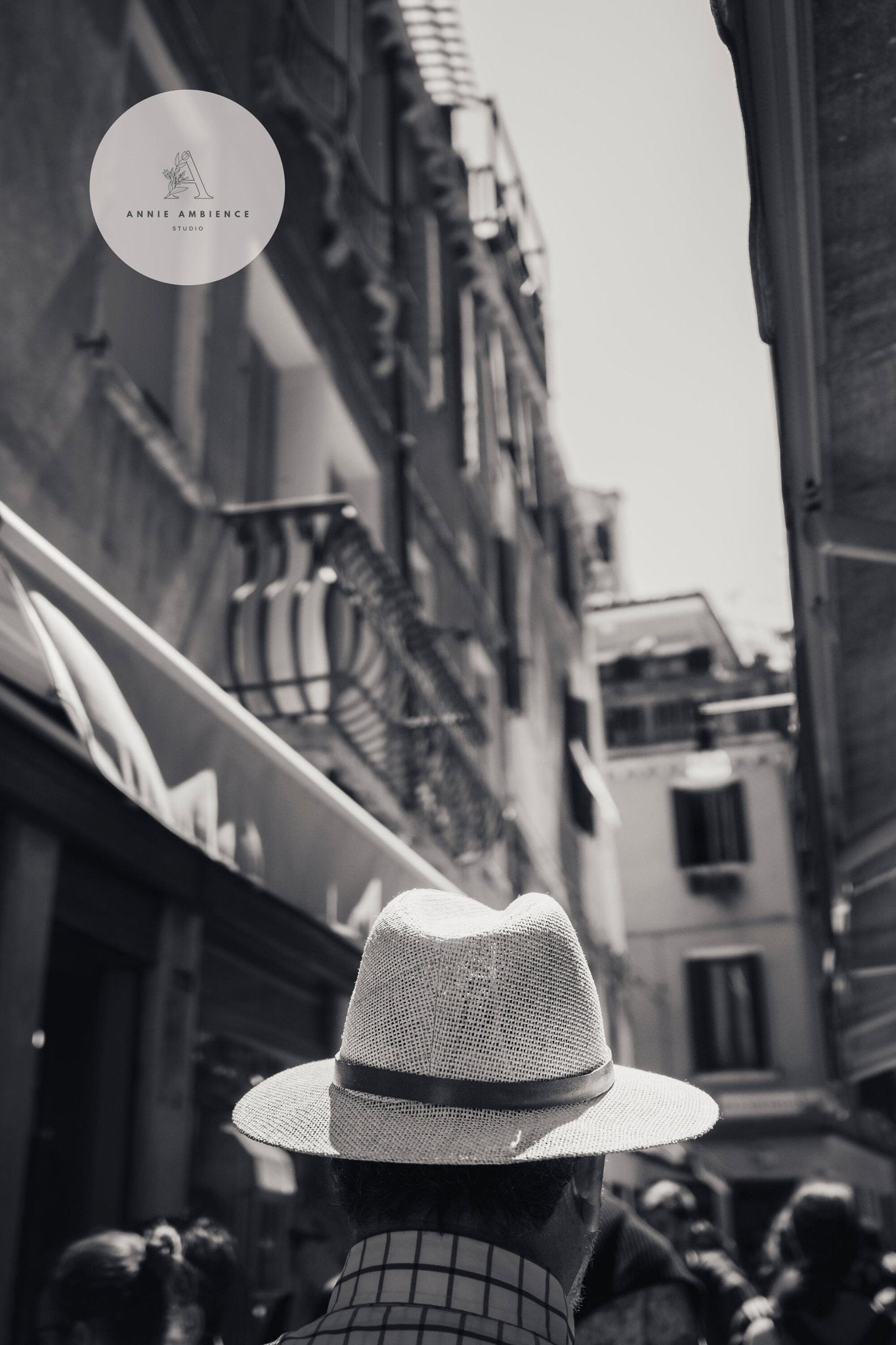 Mystery Man Black and White: Person in a hat on a narrow street with tall buildings.