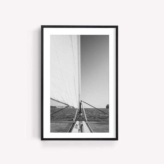 Framed on a white wall, Nautical Harmony Black and White shows a sailboats mast and sail against the sea and horizon.