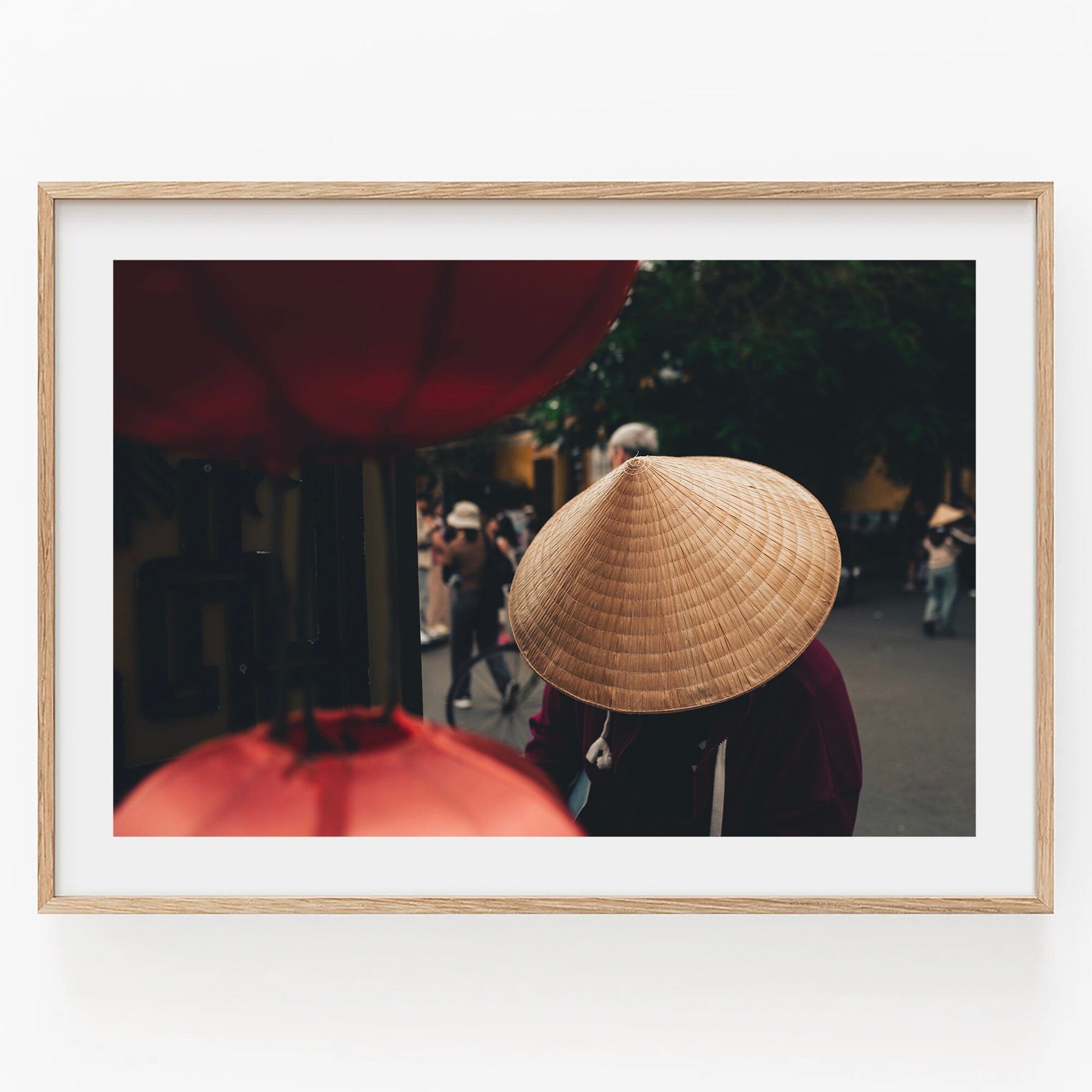 Person wearing a Nón Lá walks past large red lanterns on a street.