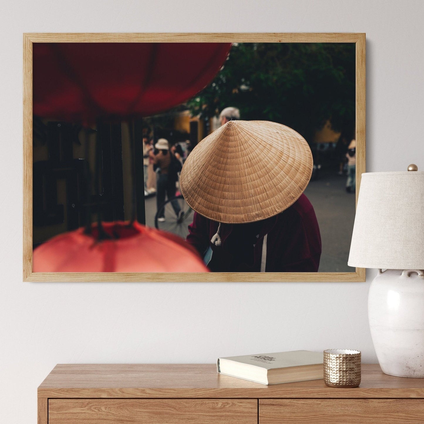 Framed Nón Lá photo on a wall above a wooden table with a lamp and book.