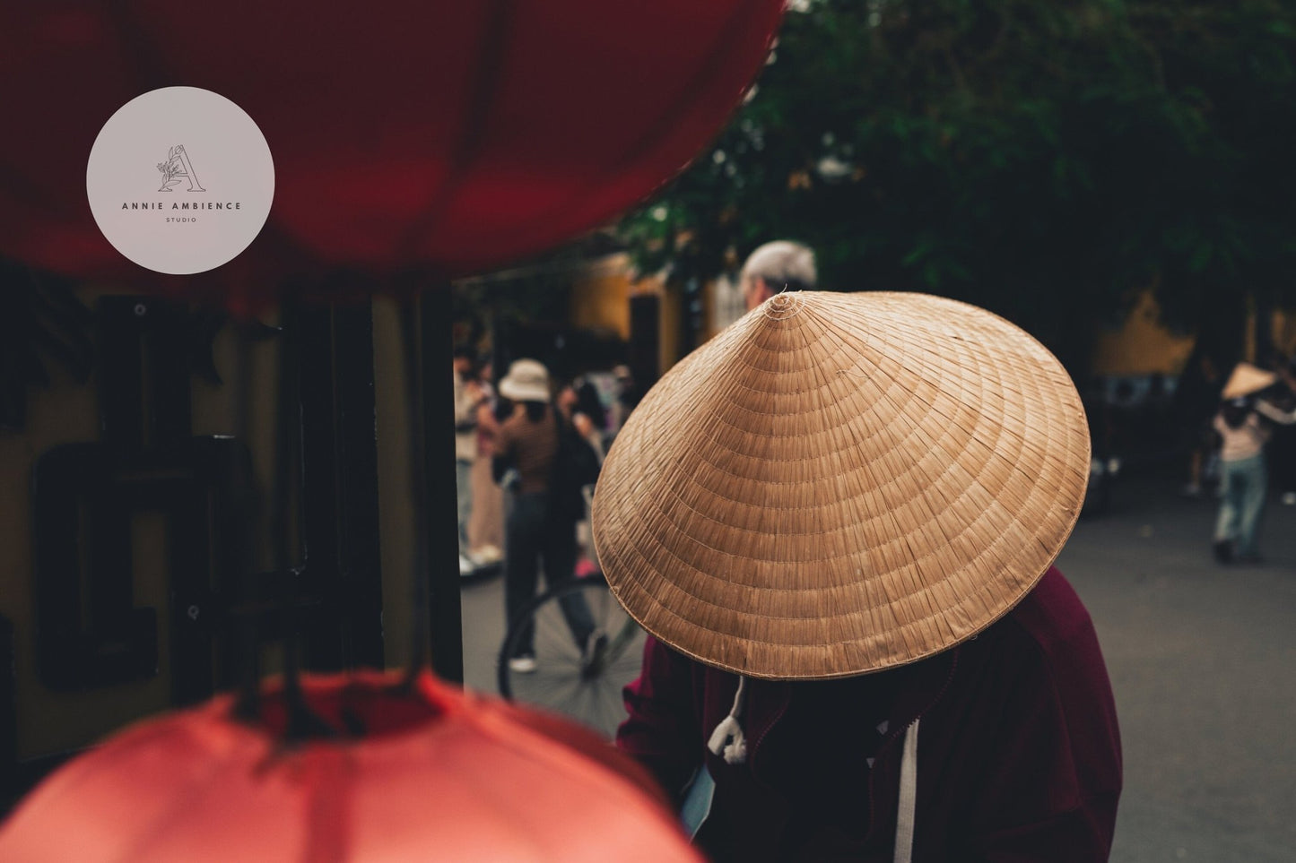 Person wearing a Nón Lá next to red lanterns on a busy street.