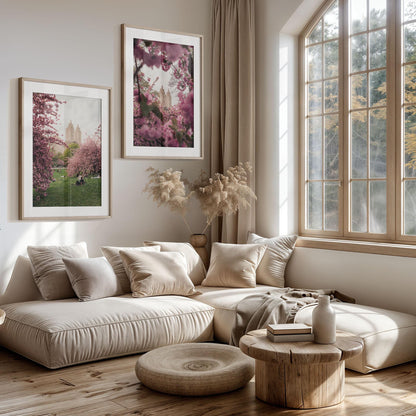 Bright living room with beige sofa, round wooden table, large window, and NYC Cherry Blossoms - Set of 2 on the wall.