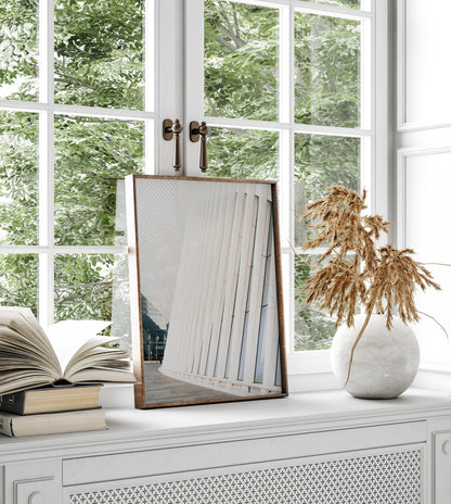 Oculus, books, and a vase on a white shelf reflect modern architecture in the mirror.