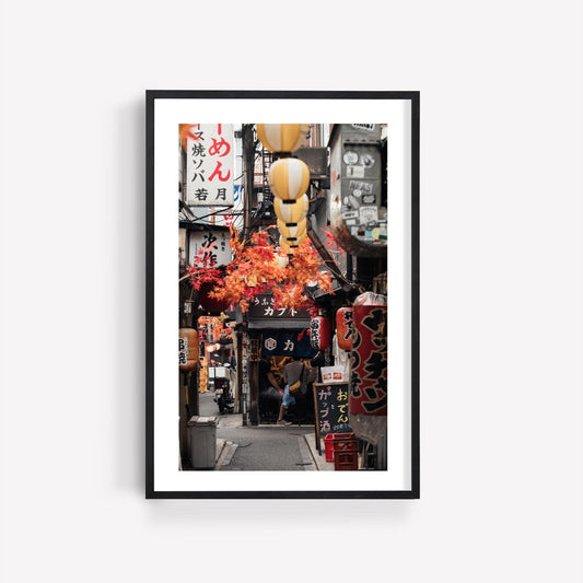 Framed photo titled Omoide Yokocho, showcasing a narrow Japanese alleyway adorned with lanterns and vibrant signs.