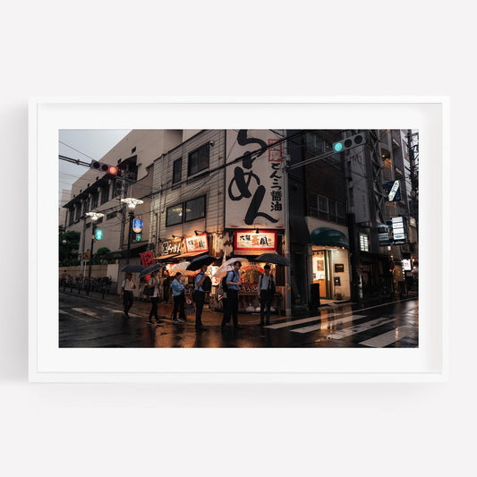 A scene of people with Osaka Drizzle umbrellas outside a ramen shop in the city, bright signs lighting up the wet pavement.