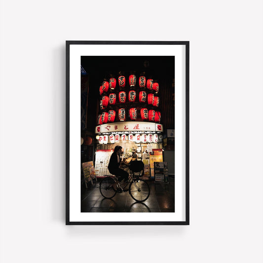 A person riding the Osaka Lantern Biker at night, surrounded by illuminated red lanterns and signs in the background.