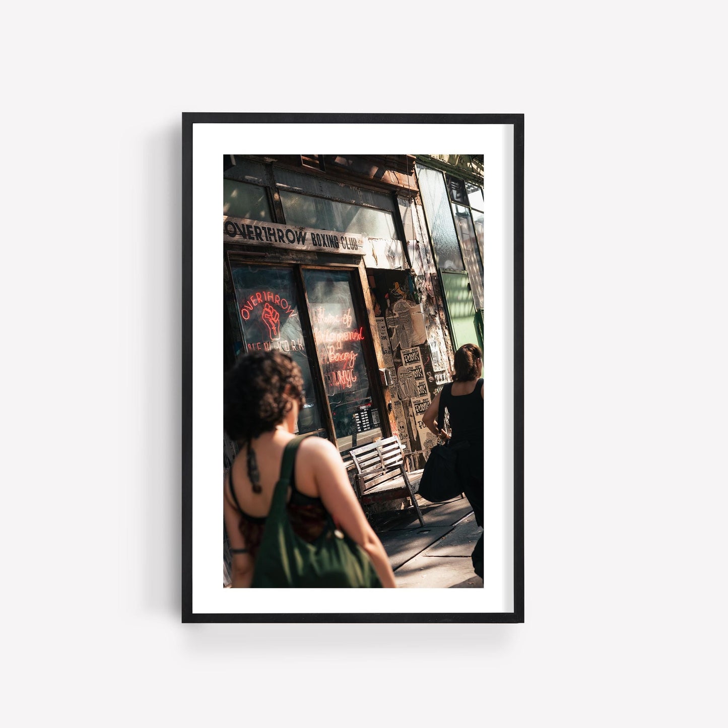 Framed photo of two women walking past the Overthrow Boxing Club storefront with various posters and signs.