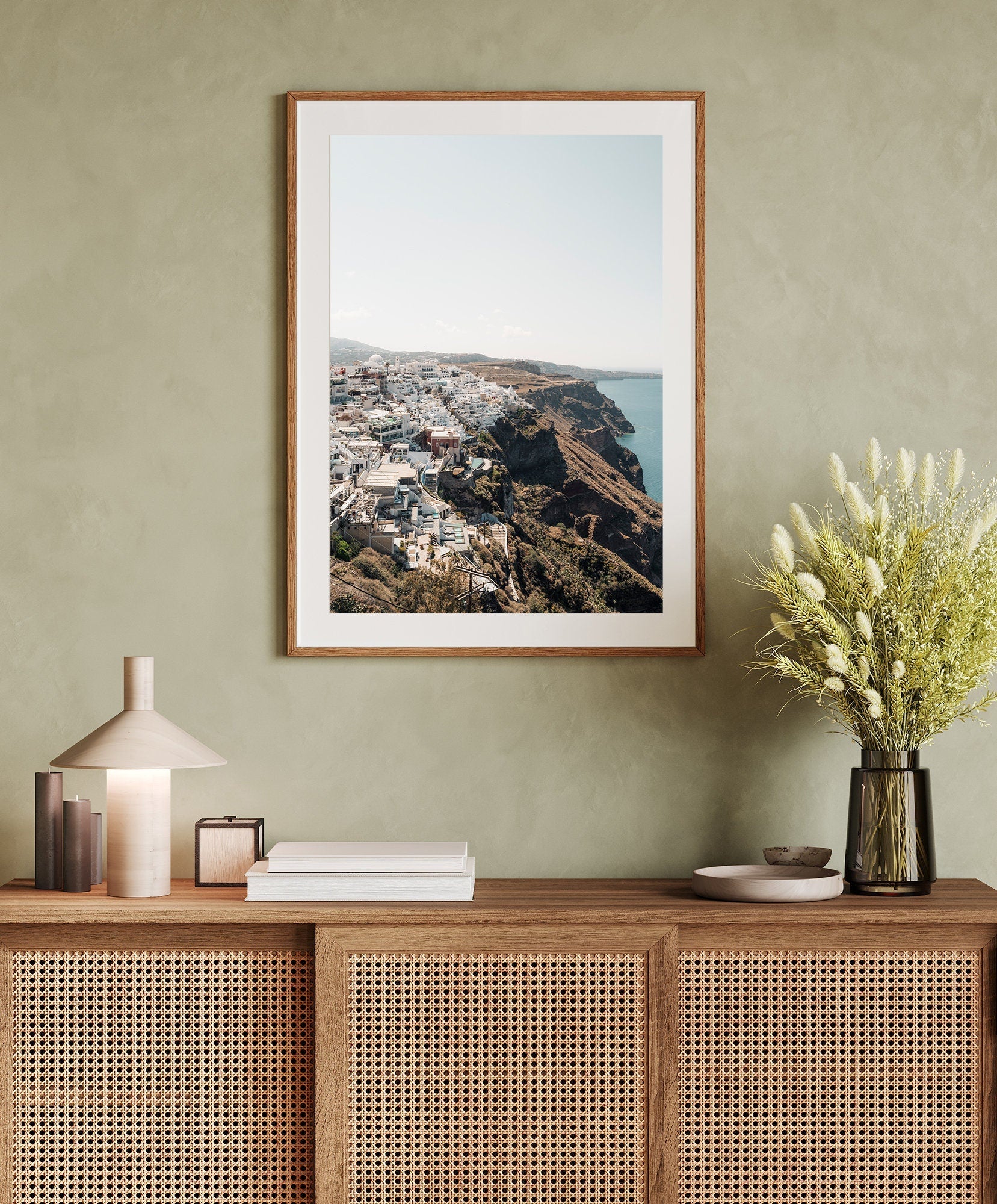 Perched coastal photo above a wooden sideboard with books, a lamp, and a flower vase.