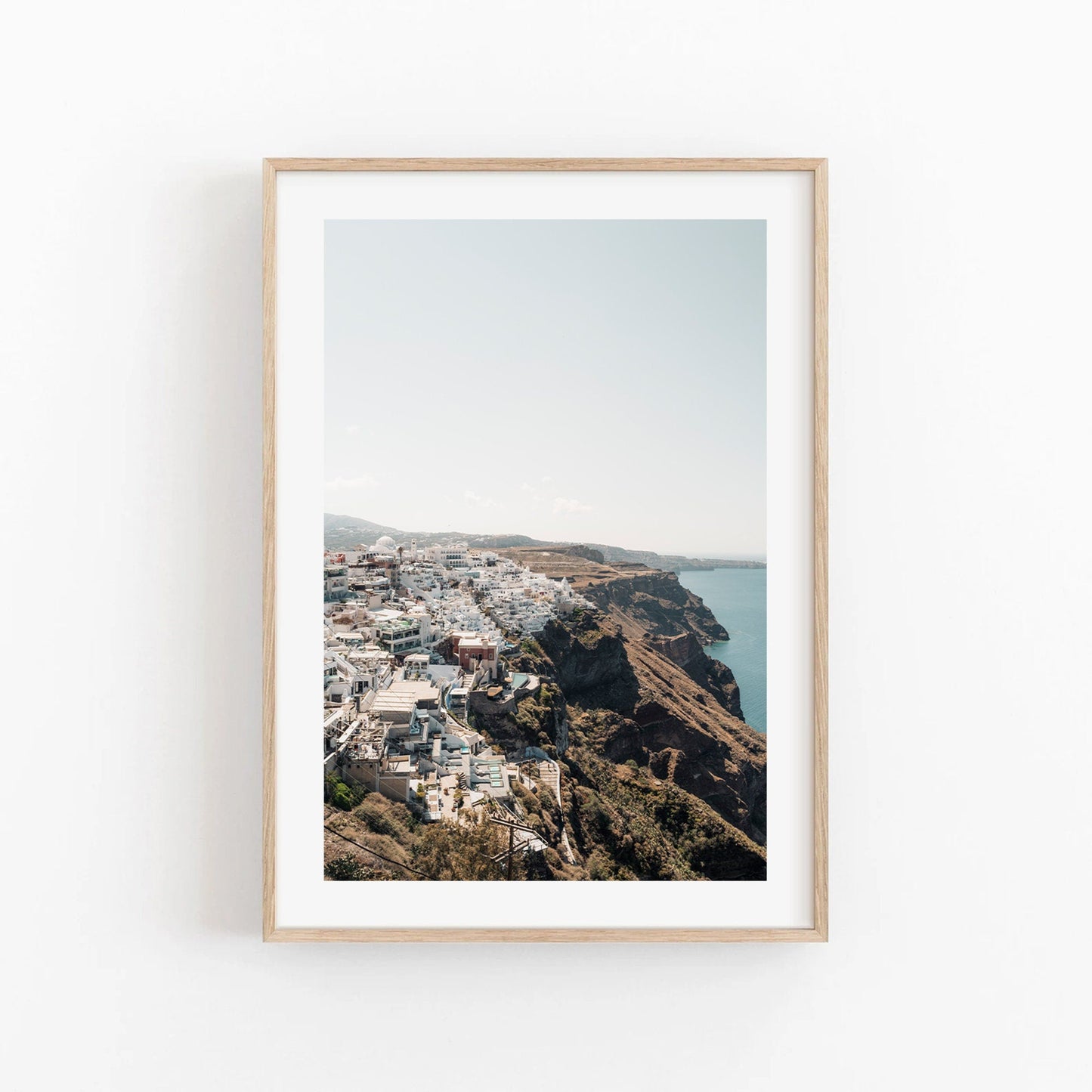 Perched: Framed photo of a coastal town with cliff-side white buildings and sea views under a clear sky.