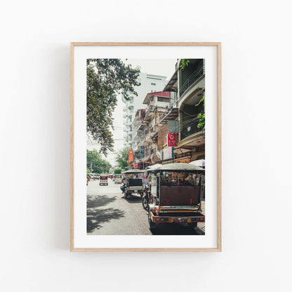 Framed Phnom Penh TukTuk photo of a busy street with tuk-tuks and buildings on a sunny day.