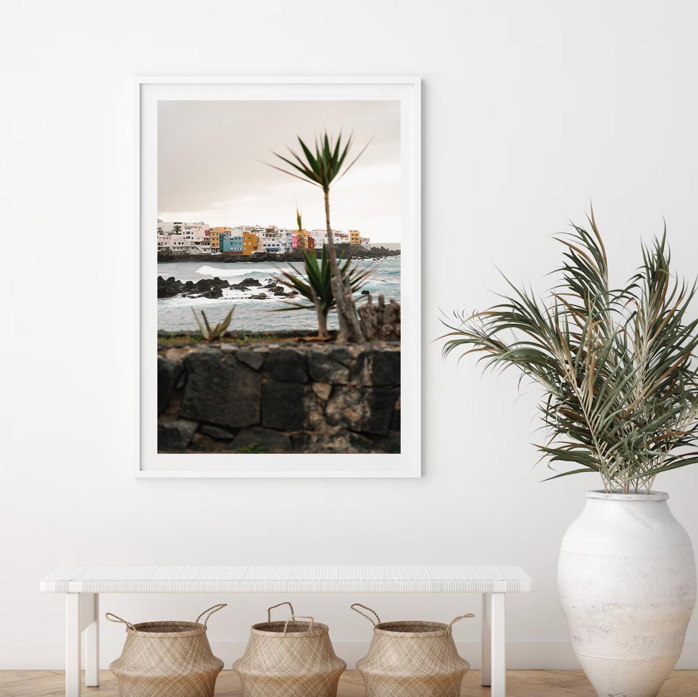 The Playa Jardín framed coastal cityscape art hangs above a bench with baskets in a minimalist room.