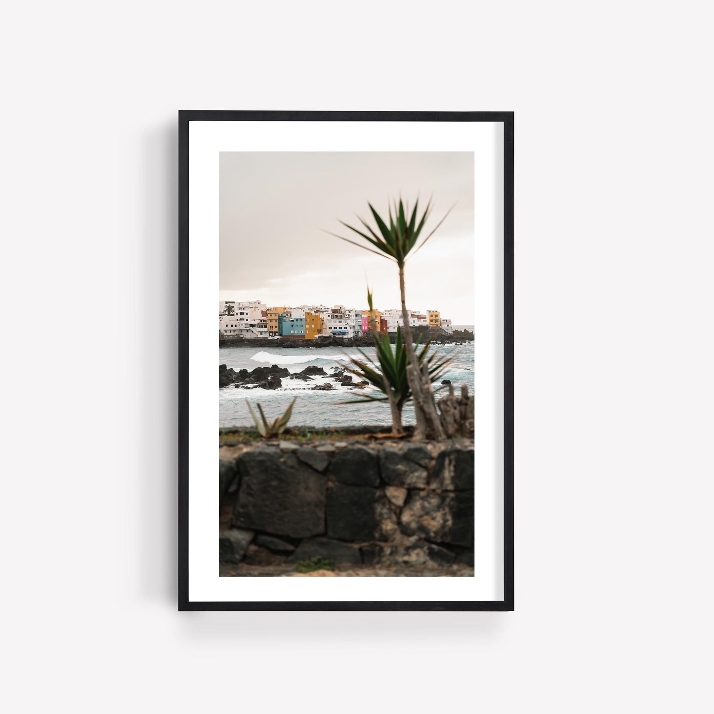 Framed photo of Playa Jardín, featuring colorful buildings, crashing waves, and a palm tree in the foreground.