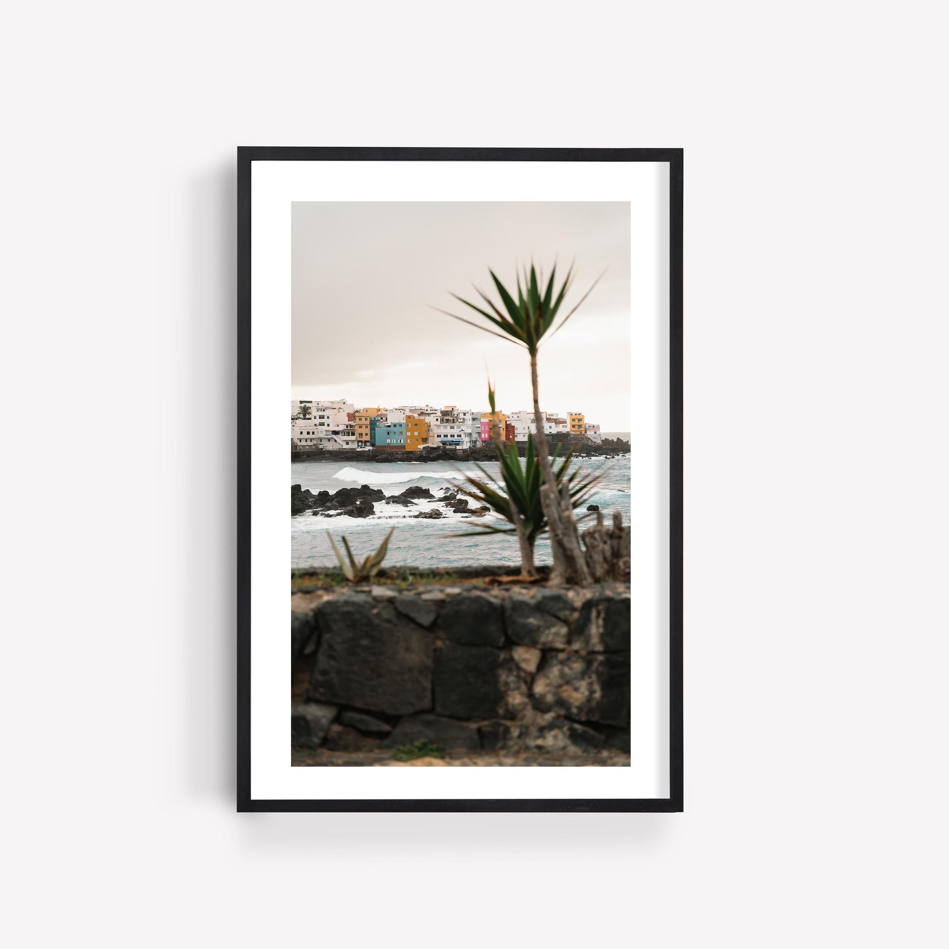 Framed photo of Playa Jardín, featuring colorful buildings, crashing waves, and a palm tree in the foreground.