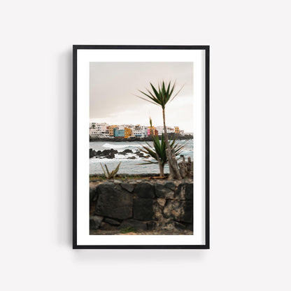 Framed photo of Playa Jardín, featuring colorful buildings, crashing waves, and a palm tree in the foreground.
