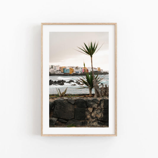 Playa Jardín framed photo: vibrant seaside buildings, palm plants, and ocean waves on a white wall.