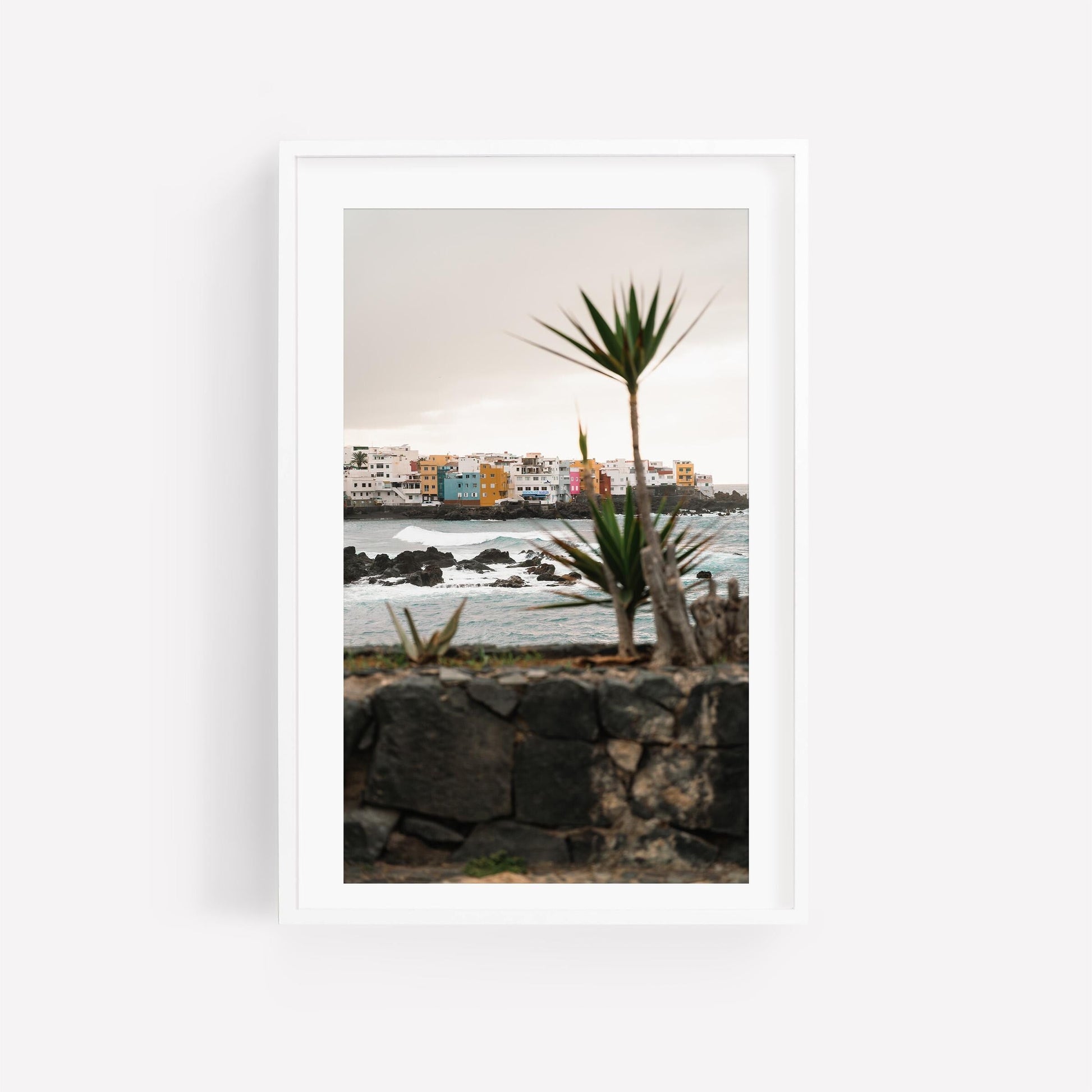 Playa Jardín features colorful buildings, ocean waves, and spiky plants in the foreground, framed in white.