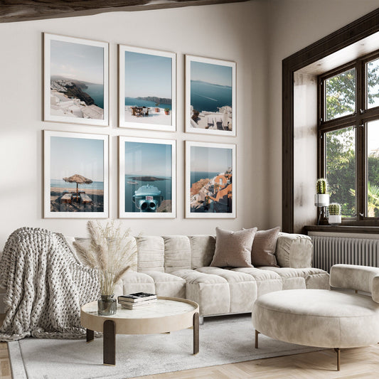 Cozy living room with a beige sectional, round ottoman, coastal wall art (Santorini Set of 6), and a large window view.