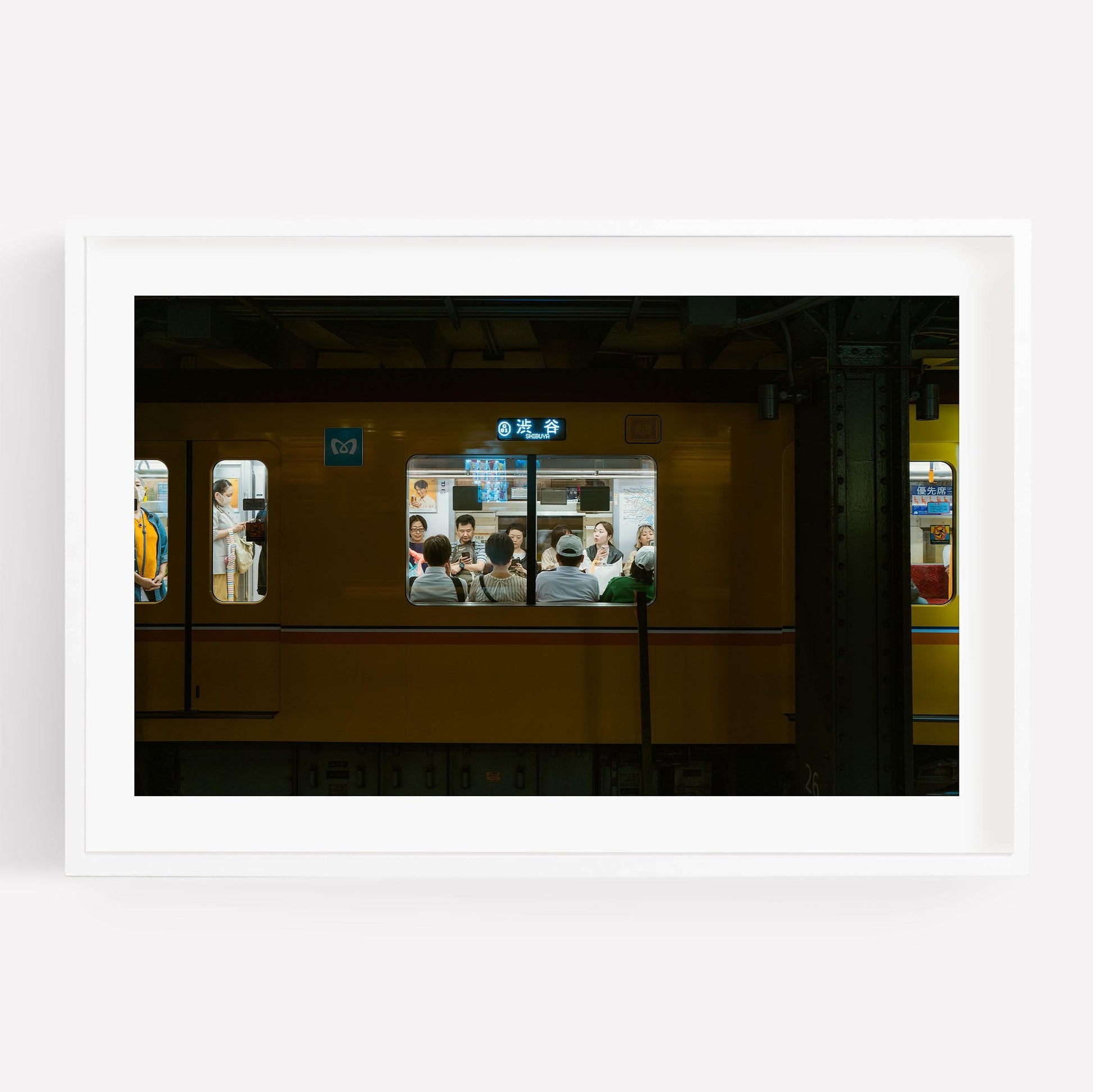 Framed photo of passengers in a yellow train, viewed through windows at Shibuya Station.