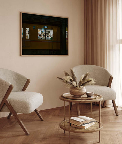 Minimalist living room featuring the Shibuya Station, two beige chairs, a small round table with books, and framed wall art.