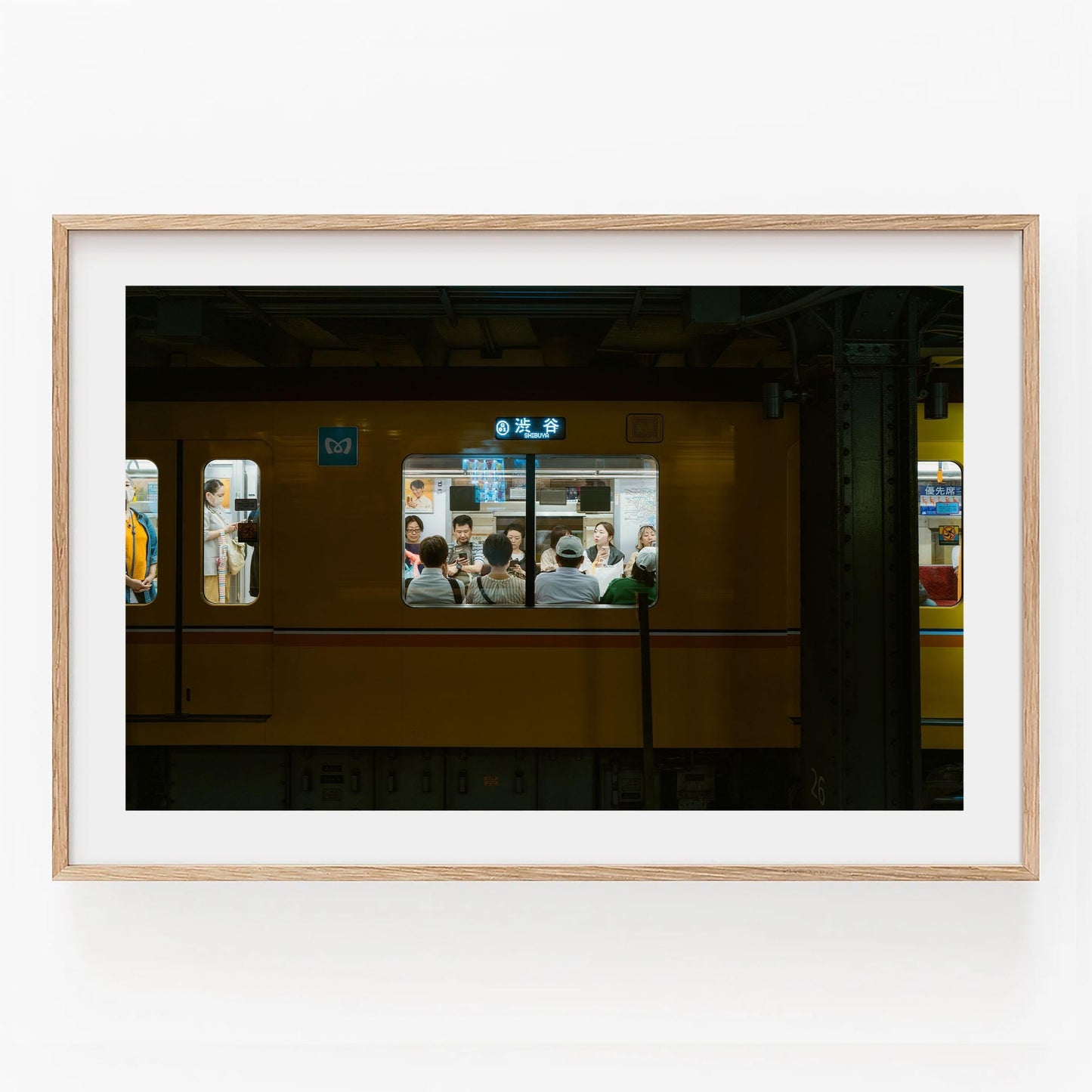 Framed photo of Shibuya Station, showing people in a yellow train carriage through the window.