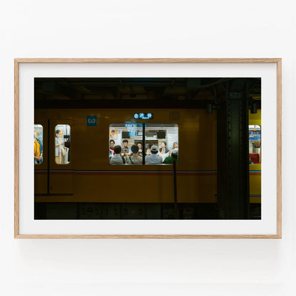 Framed photo of Shibuya Station, showing people in a yellow train carriage through the window.